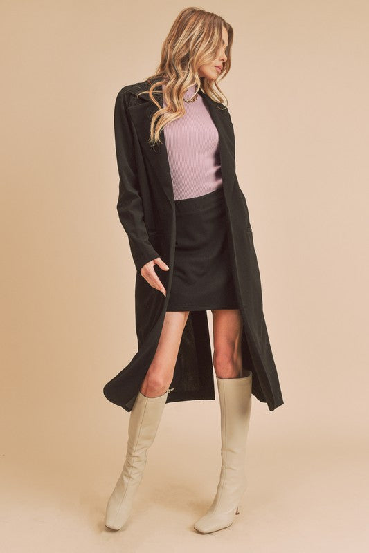 Woman wearing a black coat, pink top, black skirt, and beige knee-high boots on a beige background