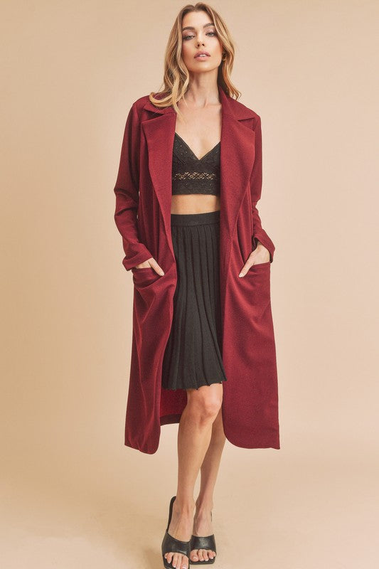 Woman wearing a burgundy coat over a black outfit on a beige background