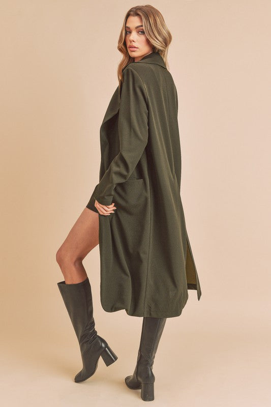 Woman wearing a long green coat and black boots on a beige background