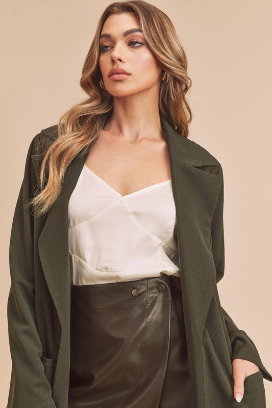 Woman wearing a green coat over a white top and black pants on a beige background