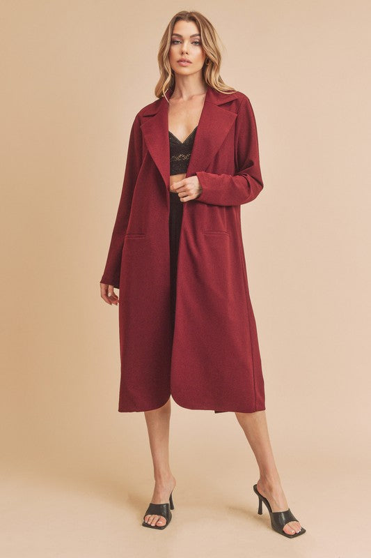 Woman wearing a long burgundy coat against a beige background