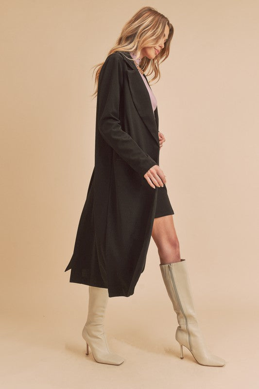 Woman wearing a long black coat and knee-high beige boots on a beige background